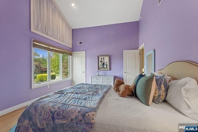 bedroom with high vaulted ceiling, baseboards, wood finished floors, and visible vents