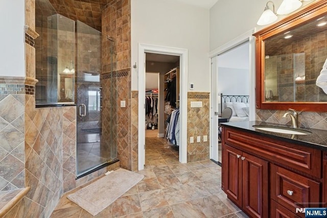 bathroom featuring vanity, tile walls, a walk in closet, a wainscoted wall, and a stall shower