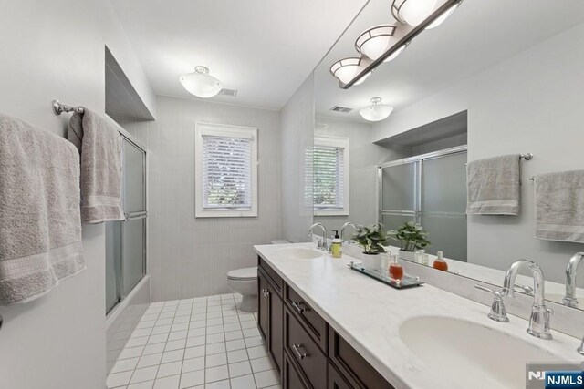 bathroom with a sink, tile patterned floors, a shower with shower door, and visible vents