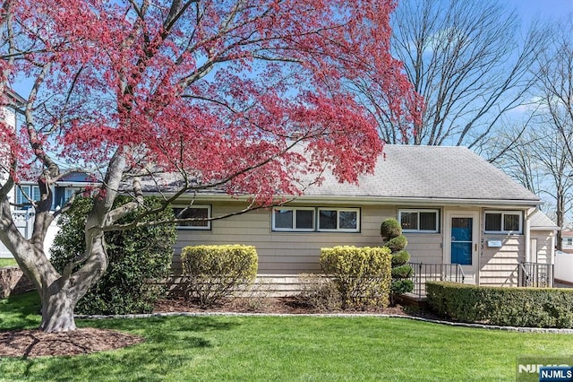 ranch-style house featuring roof with shingles and a front lawn