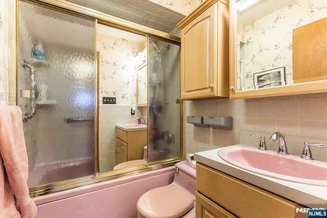 full bath featuring vanity, tile walls, combined bath / shower with glass door, and wallpapered walls