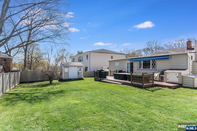 rear view of property with a deck, an outdoor structure, a fenced backyard, a shed, and a yard