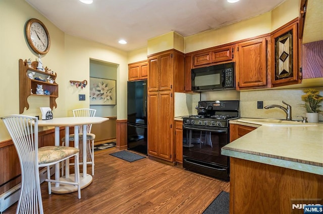 kitchen featuring brown cabinets, dark wood-style flooring, a sink, light countertops, and black appliances
