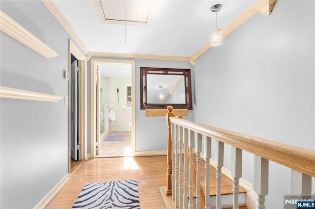 hall featuring light wood-style floors, attic access, baseboards, and an upstairs landing