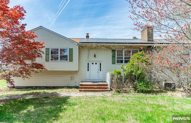 exterior space featuring a lawn, solar panels, central AC unit, and a chimney