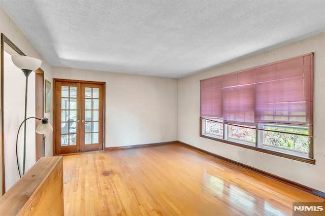 unfurnished room featuring french doors, a textured ceiling, wood finished floors, and a wealth of natural light