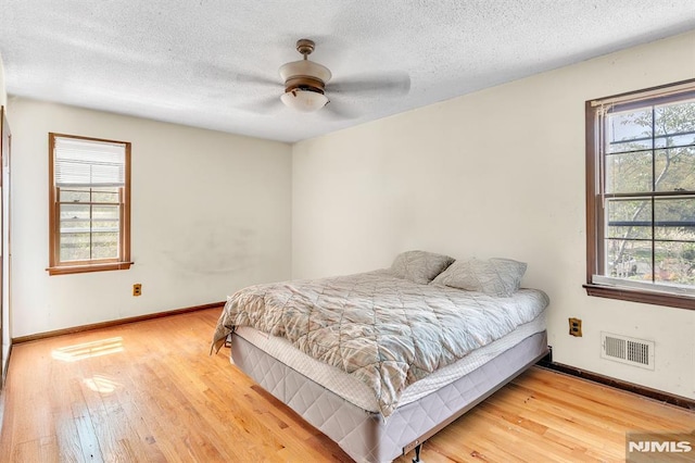 bedroom with a textured ceiling, baseboards, visible vents, and wood finished floors