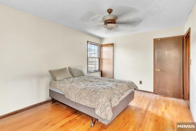 bedroom with light wood-style floors, baseboards, and a textured ceiling