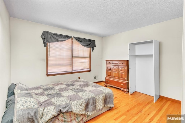 bedroom featuring baseboards, a textured ceiling, visible vents, and light wood-style flooring