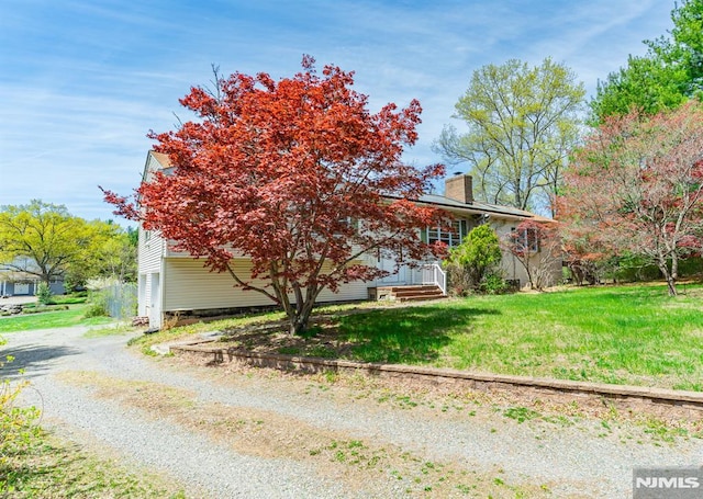 view of property exterior with a yard, driveway, and a chimney
