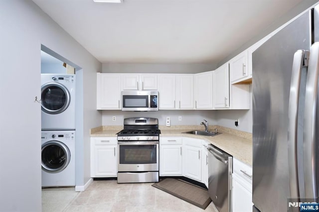kitchen with a sink, appliances with stainless steel finishes, white cabinets, and stacked washer / dryer
