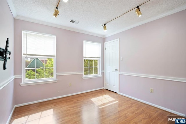 spare room featuring visible vents, rail lighting, wood finished floors, and ornamental molding