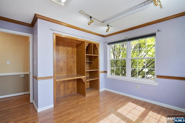 interior space featuring track lighting, ornamental molding, a textured ceiling, and wood finished floors