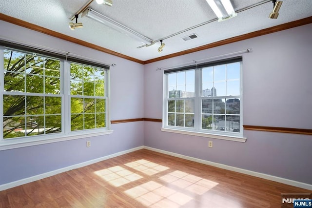 spare room featuring visible vents, rail lighting, wood finished floors, and ornamental molding