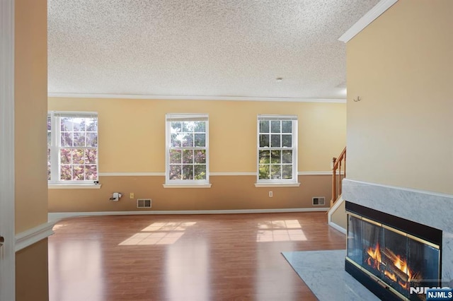 unfurnished living room featuring crown molding, a textured ceiling, wood finished floors, and visible vents