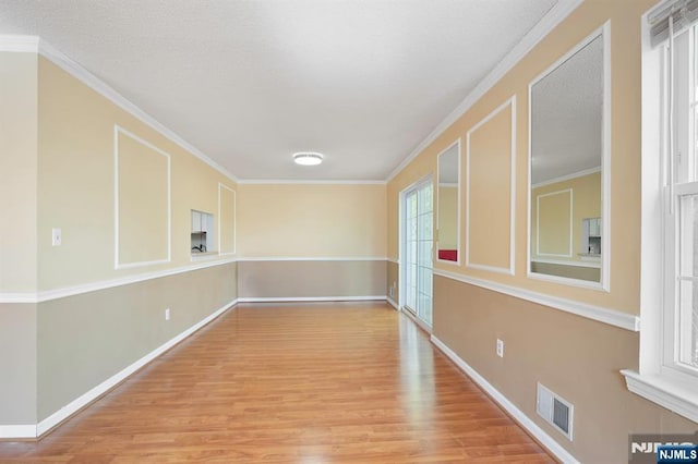 unfurnished room featuring visible vents, ornamental molding, baseboards, and wood finished floors