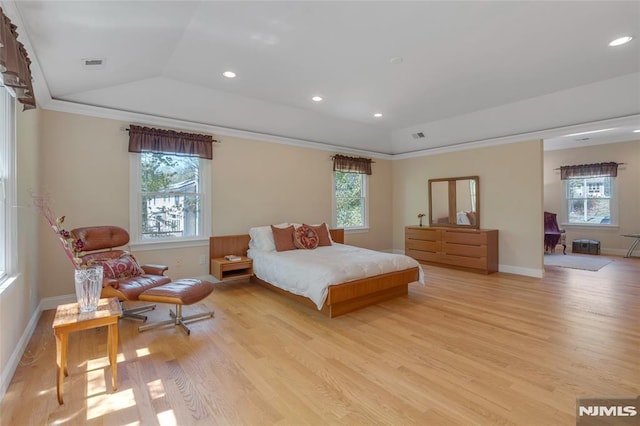 bedroom with light wood-type flooring, a tray ceiling, multiple windows, and visible vents