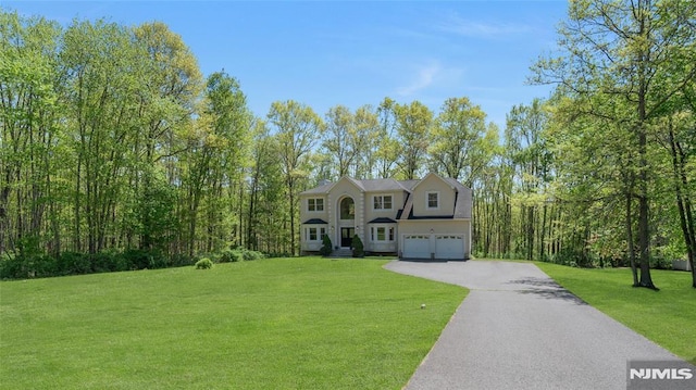 colonial house featuring an attached garage, a front lawn, and aphalt driveway