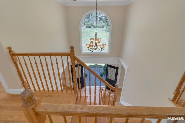 stairs with crown molding, baseboards, a notable chandelier, and wood finished floors