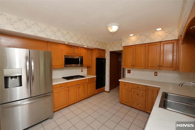 kitchen featuring a sink, light countertops, stainless steel appliances, and wallpapered walls