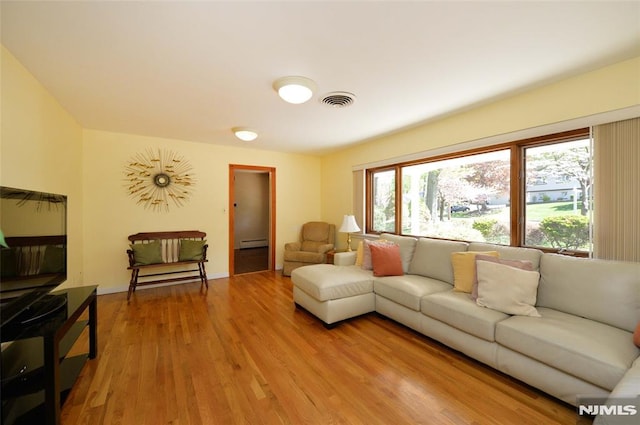 living area with visible vents, light wood finished floors, and a baseboard heating unit