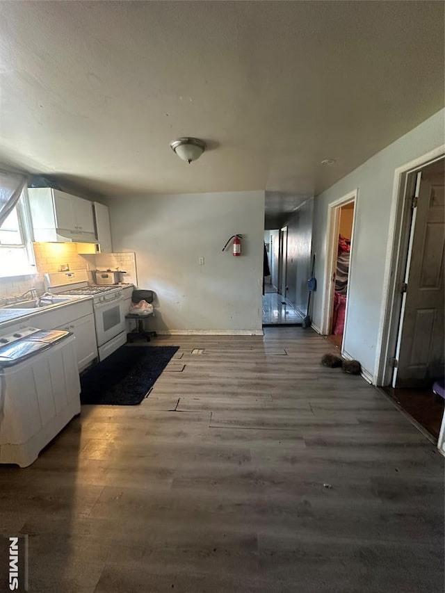 kitchen with white gas range, white cabinets, wood finished floors, a sink, and tasteful backsplash