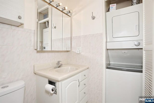 half bathroom featuring tile walls, stacked washer / drying machine, vanity, and toilet