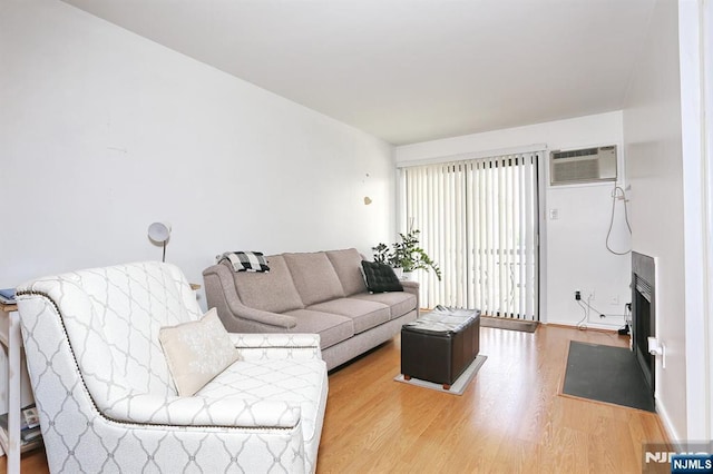 living room featuring a fireplace with flush hearth, a wall unit AC, and wood finished floors