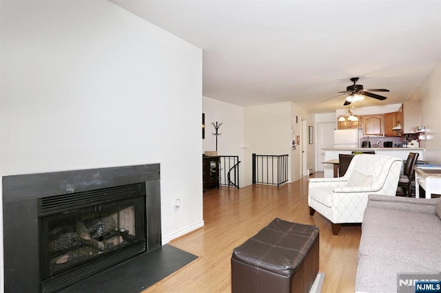 living room featuring light wood-style floors, a ceiling fan, baseboards, and a glass covered fireplace