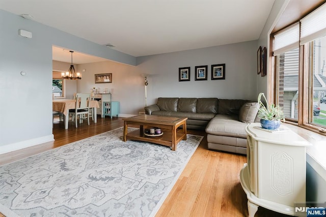 living room with baseboards, an inviting chandelier, and light wood-type flooring