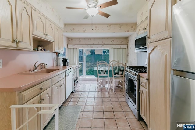 kitchen featuring ceiling fan, appliances with stainless steel finishes, a sink, light countertops, and wallpapered walls