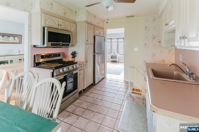 kitchen with a sink, a ceiling fan, stainless steel appliances, and wallpapered walls