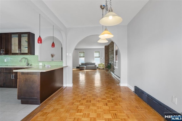 kitchen with light countertops, arched walkways, baseboards, and dark brown cabinets