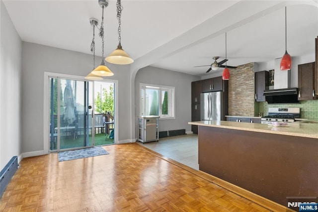 kitchen with light countertops, wall chimney exhaust hood, stainless steel appliances, a ceiling fan, and tasteful backsplash