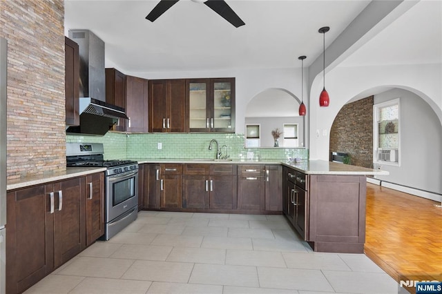 kitchen with a sink, stainless steel gas stove, wall chimney exhaust hood, a peninsula, and a ceiling fan