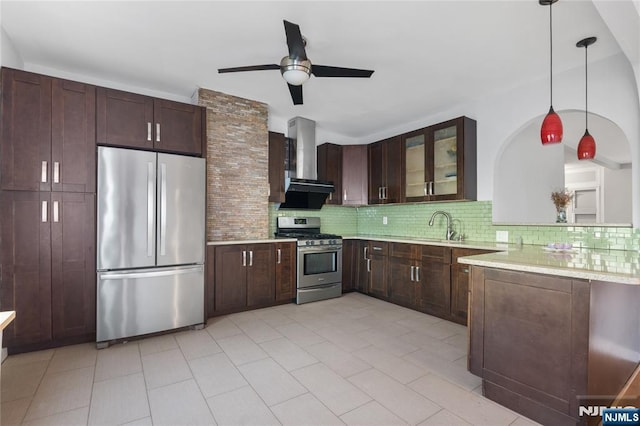 kitchen featuring light countertops, wall chimney exhaust hood, stainless steel appliances, a ceiling fan, and decorative backsplash