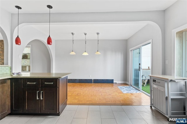 kitchen featuring arched walkways, hanging light fixtures, and dark brown cabinets