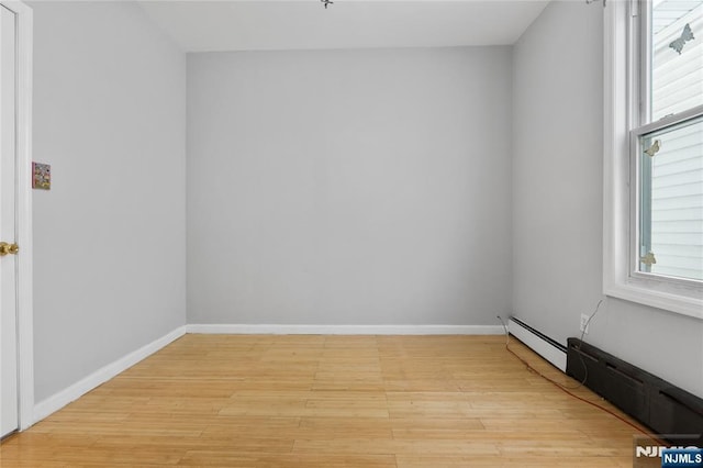 empty room featuring baseboards, wood finished floors, a wealth of natural light, and baseboard heating