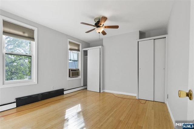 unfurnished bedroom with a baseboard heating unit, wood finished floors, multiple windows, and two closets