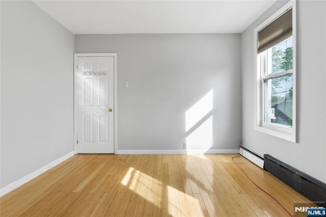 spare room featuring light wood-style floors, a baseboard radiator, and baseboards