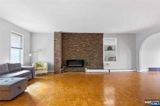 living room with a healthy amount of sunlight, arched walkways, a baseboard heating unit, and a stone fireplace