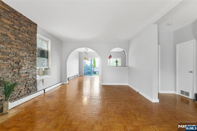 spare room with arched walkways, baseboards, a baseboard heating unit, and visible vents