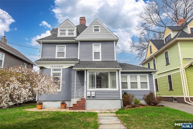 view of front of home featuring roof with shingles, a front yard, a chimney, and entry steps
