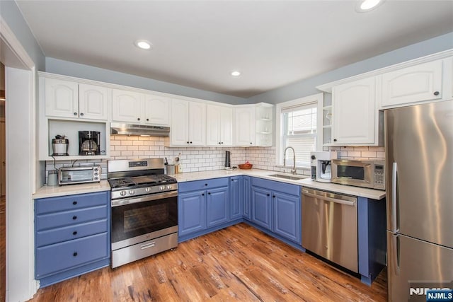 kitchen with open shelves, a sink, stainless steel appliances, under cabinet range hood, and blue cabinets