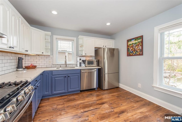 kitchen with open shelves, white cabinetry, stainless steel appliances, a sink, and blue cabinetry