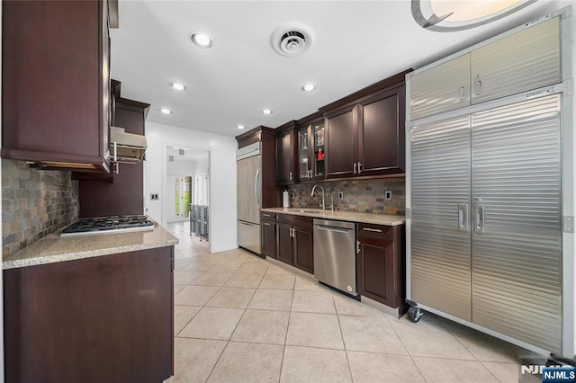 kitchen featuring decorative backsplash, dark brown cabinetry, appliances with stainless steel finishes, a sink, and light tile patterned flooring