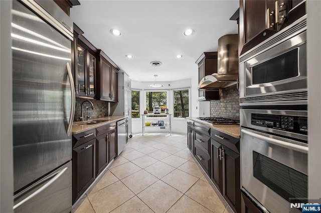 kitchen featuring recessed lighting, wall chimney exhaust hood, tasteful backsplash, a sink, and stainless steel appliances