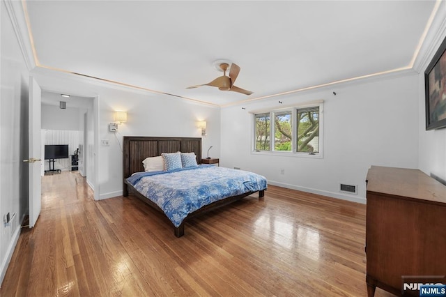 bedroom with a ceiling fan, baseboards, wood finished floors, visible vents, and ornamental molding