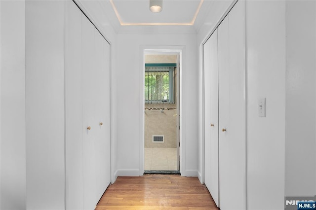 corridor with light wood-style floors, ornamental molding, and visible vents