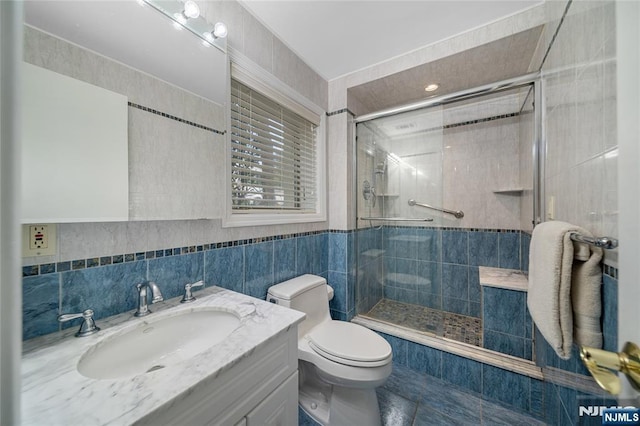 full bathroom featuring vanity, tile walls, toilet, and a shower stall